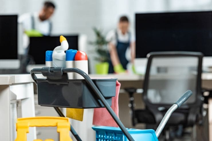 Black Mountain Cleaners equipment cart with cleaning supplies in a modern office, with team members cleaning workstations in the background.